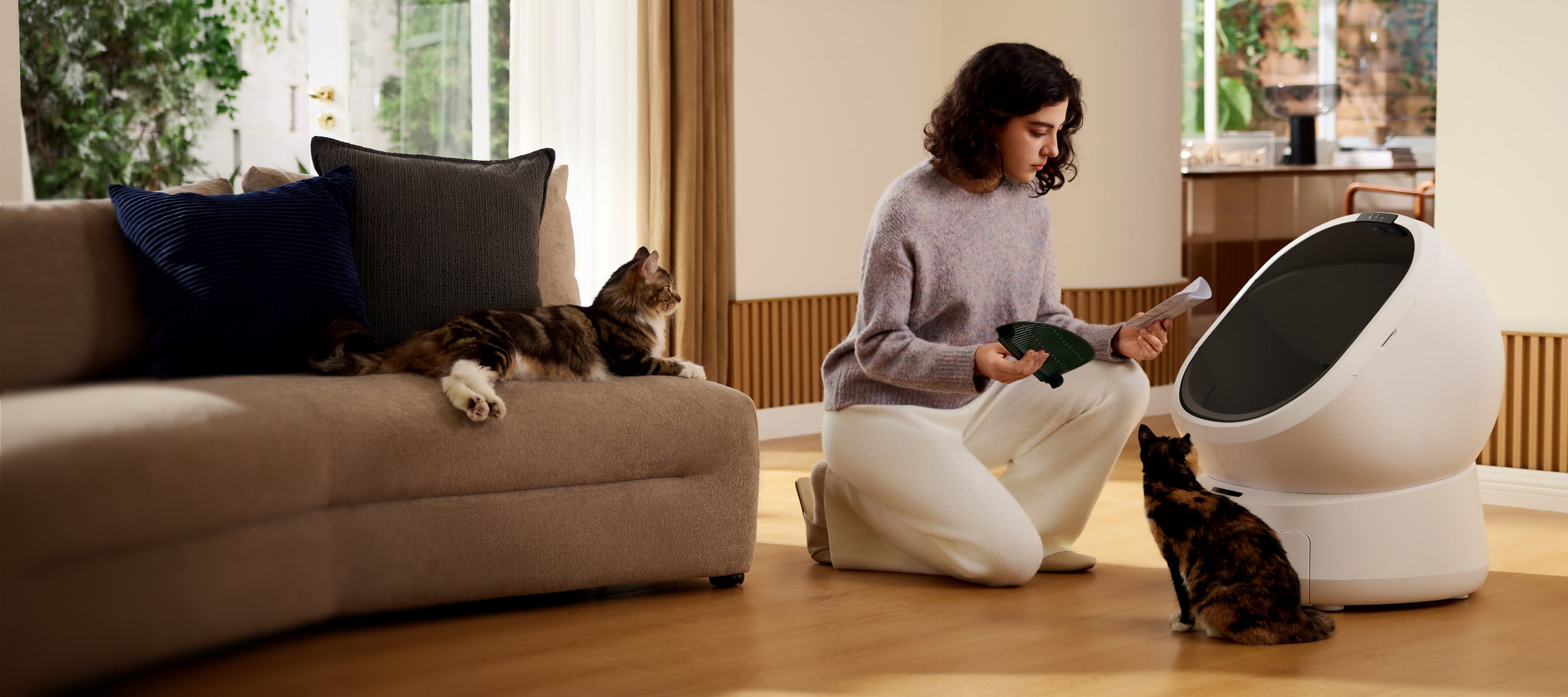 Petlibro automatic self-cleaning white cat litter box with a woman and two cats in a modern living room setting